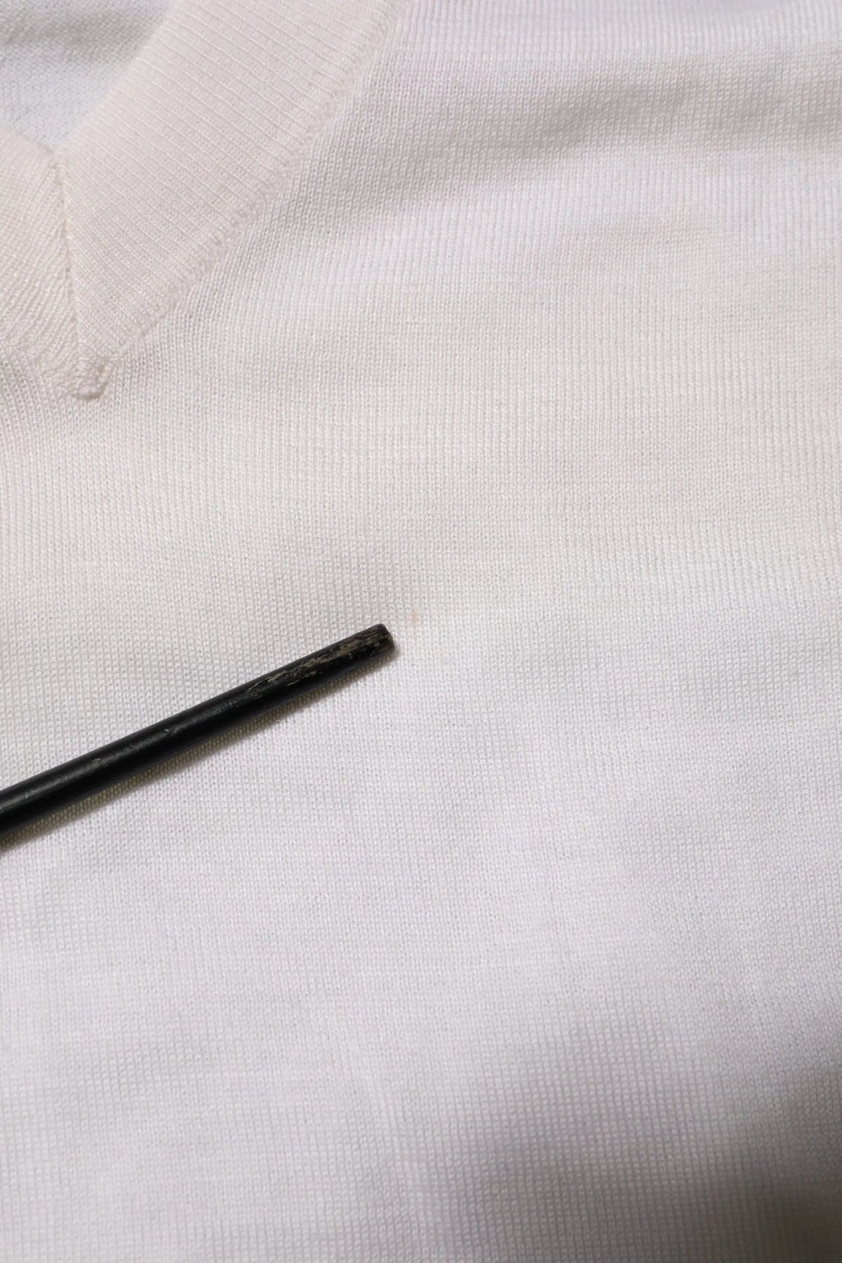 Objet cylindrique noir posé sur tissu blanc texturé avec pull dolce & gabbana en cachemire blanc col en v logo