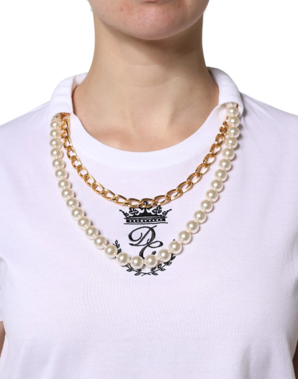 Collier double couche avec chaîne dorée et perles ivoire porté sur t shirt blanc en coton dolce gabbana avec logo couronne noir