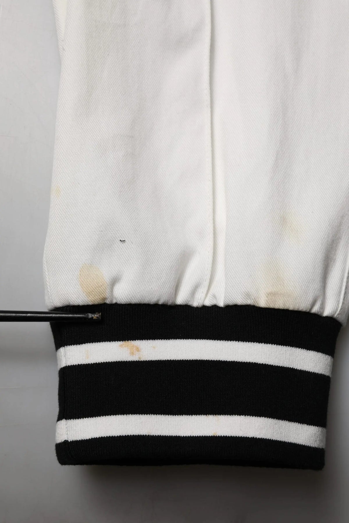 Manche de veste varsity blanche dolce & gabbana avec bord rayé noir et blanc montrant des signes d’usure