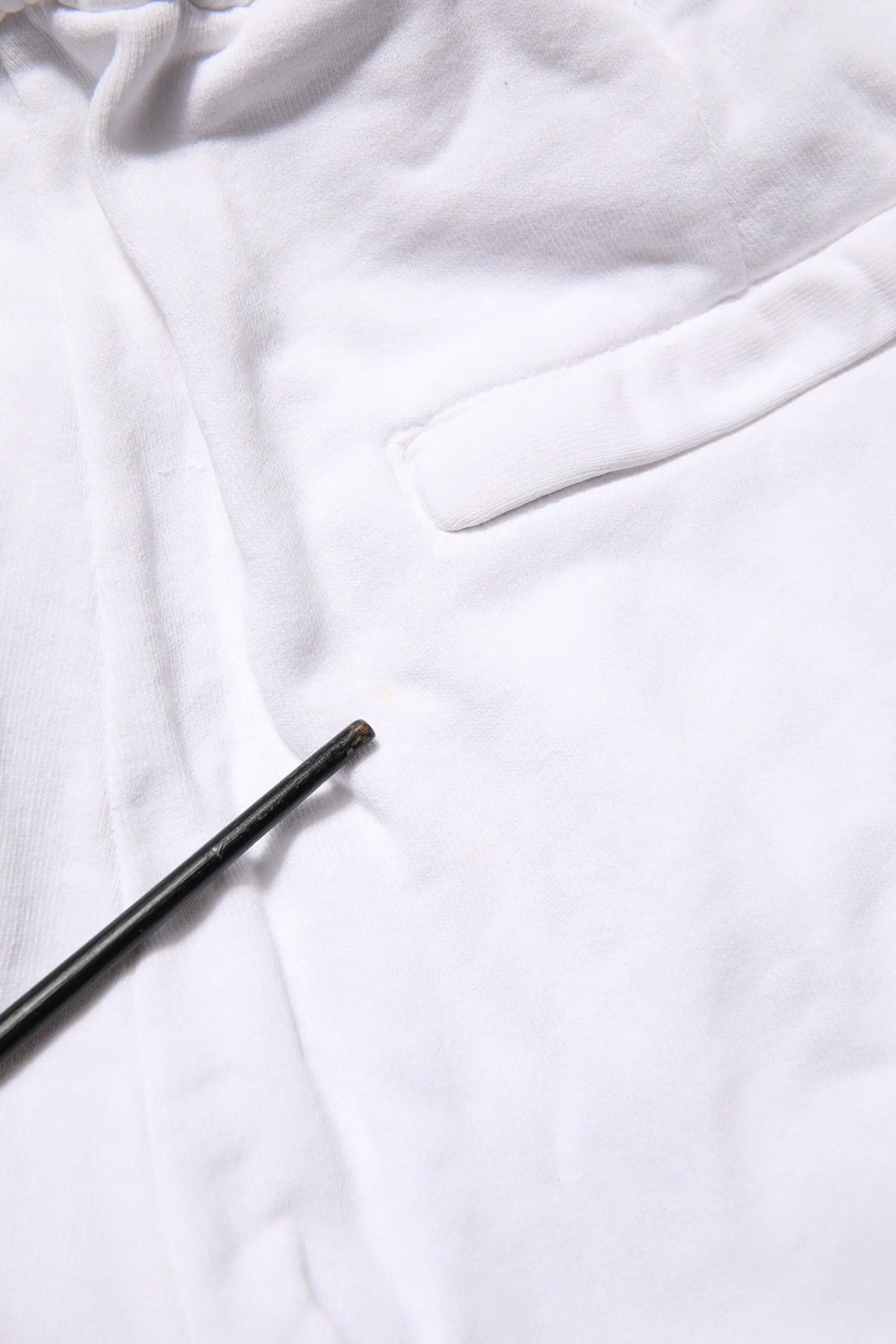 Un crayon noir fin repose en diagonale sur un tissu blanc doux à côté d un pantalon cargo blanc en coton dolce & gabbana