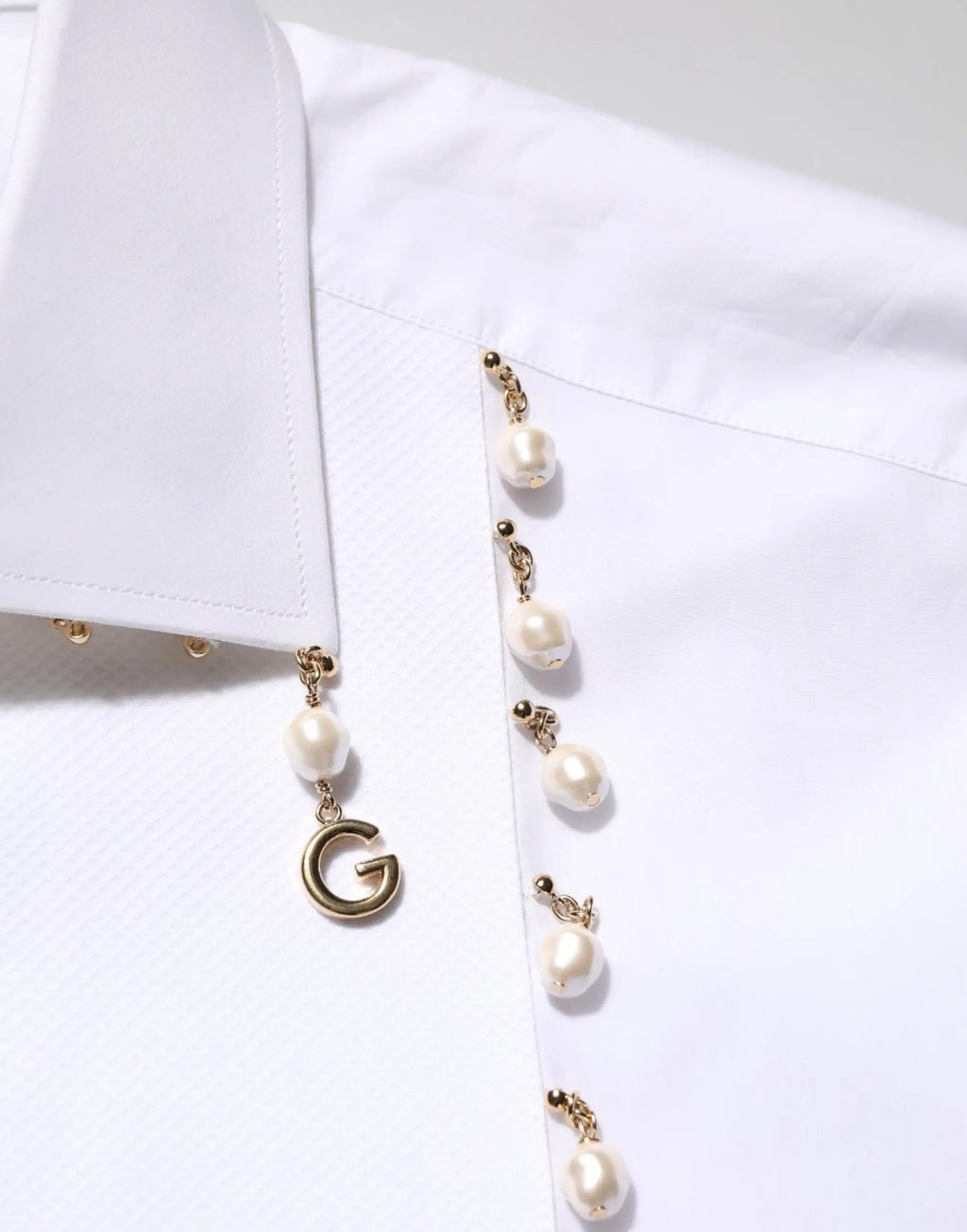 Une blouse blanche dolce gabbana en coton avec un pendentif perle doré et un charme g suspendu aux boutonnières