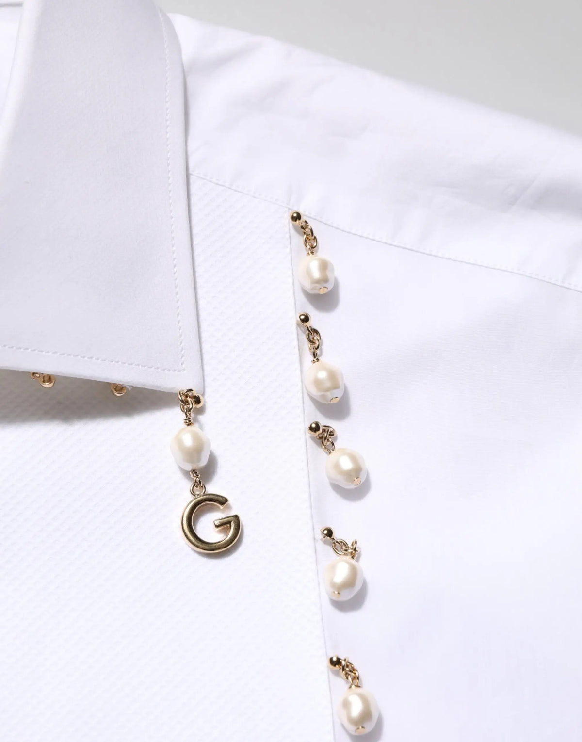 Une blouse blanche dolce gabbana en coton avec un pendentif perle doré et un charme g suspendu aux boutonnières