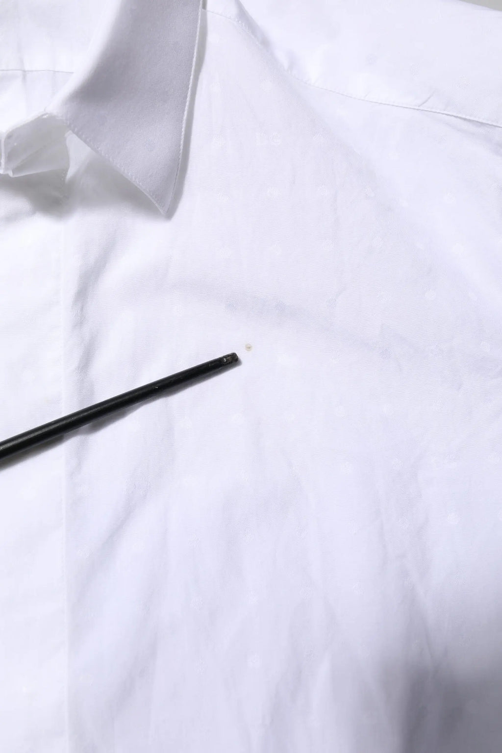 Un crayon noir repose en diagonale sur une chemise formelle blanche en coton dolce gabbana gold