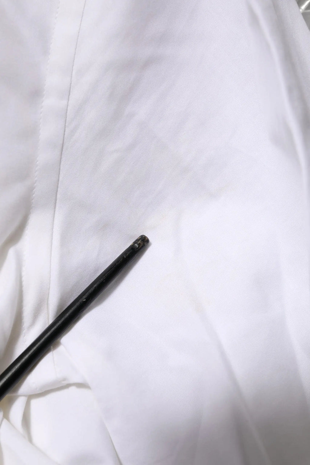 Objet cylindrique noir texturé posé sur tissu blanc avec chemise en coton blanc à manches longues gold de Dolce & Gabbana