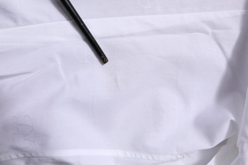 Un outil noir et mince avec une pointe légèrement usée repose en diagonale sur la chemise formelle blanche en coton à manches longues dolce gabbana gold