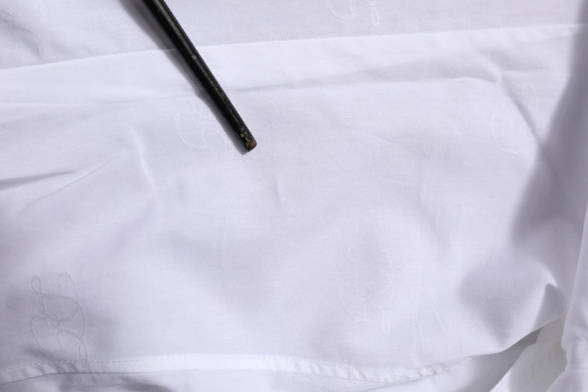 Un outil noir et mince avec une pointe légèrement usée repose en diagonale sur la chemise formelle blanche en coton à manches longues dolce gabbana gold