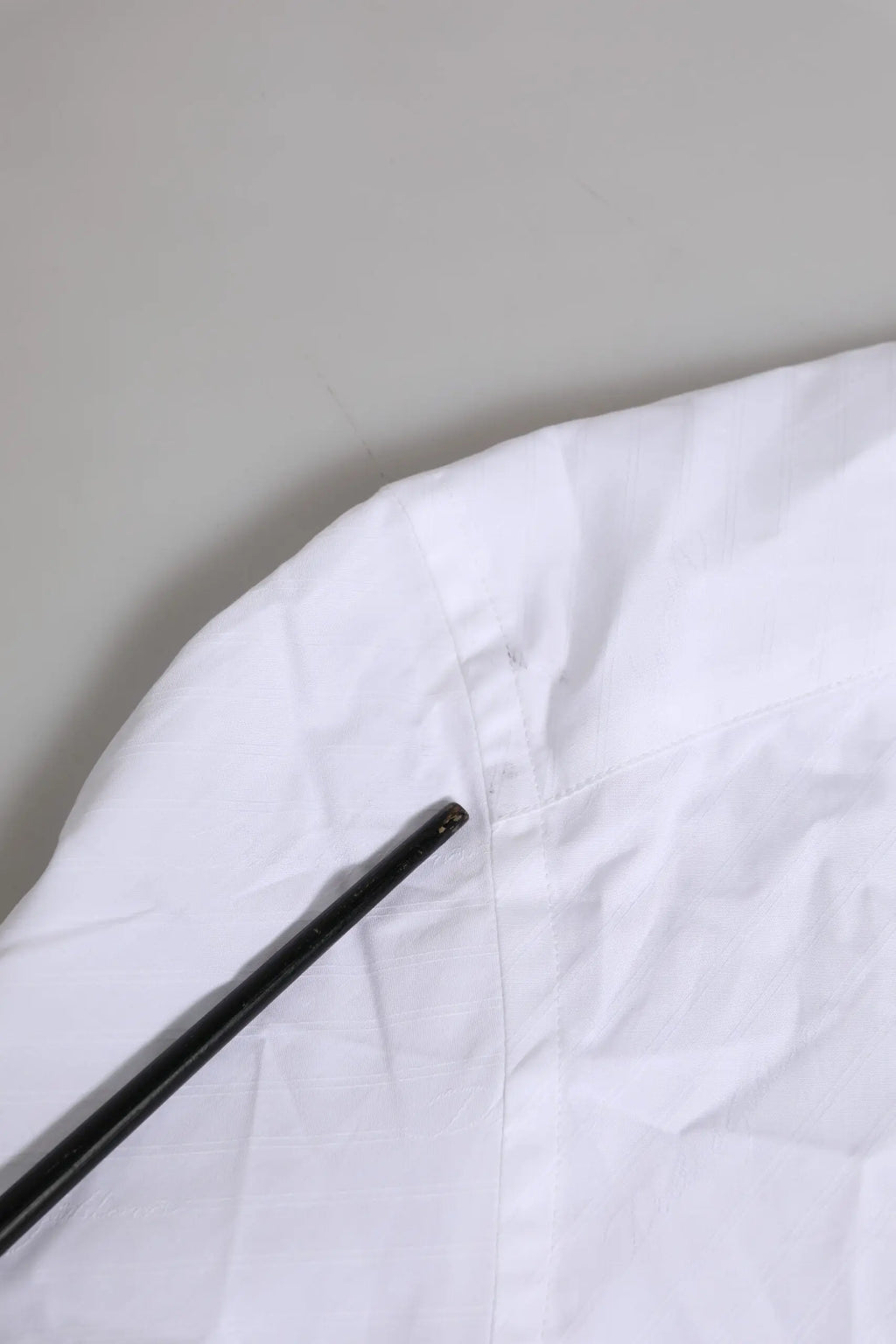 Un repose-baguettes noir élégant posé en diagonale sur un tissu blanc froissé dans une chemise formelle blanche en coton dolce gabbana