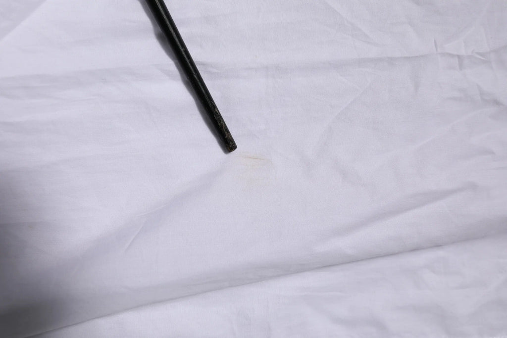 Une baguette noire élégante avec une surface lisse repose sur un tissu blanc à côté d’une chemise formelle blanche en coton dolce & gabbana manches longues