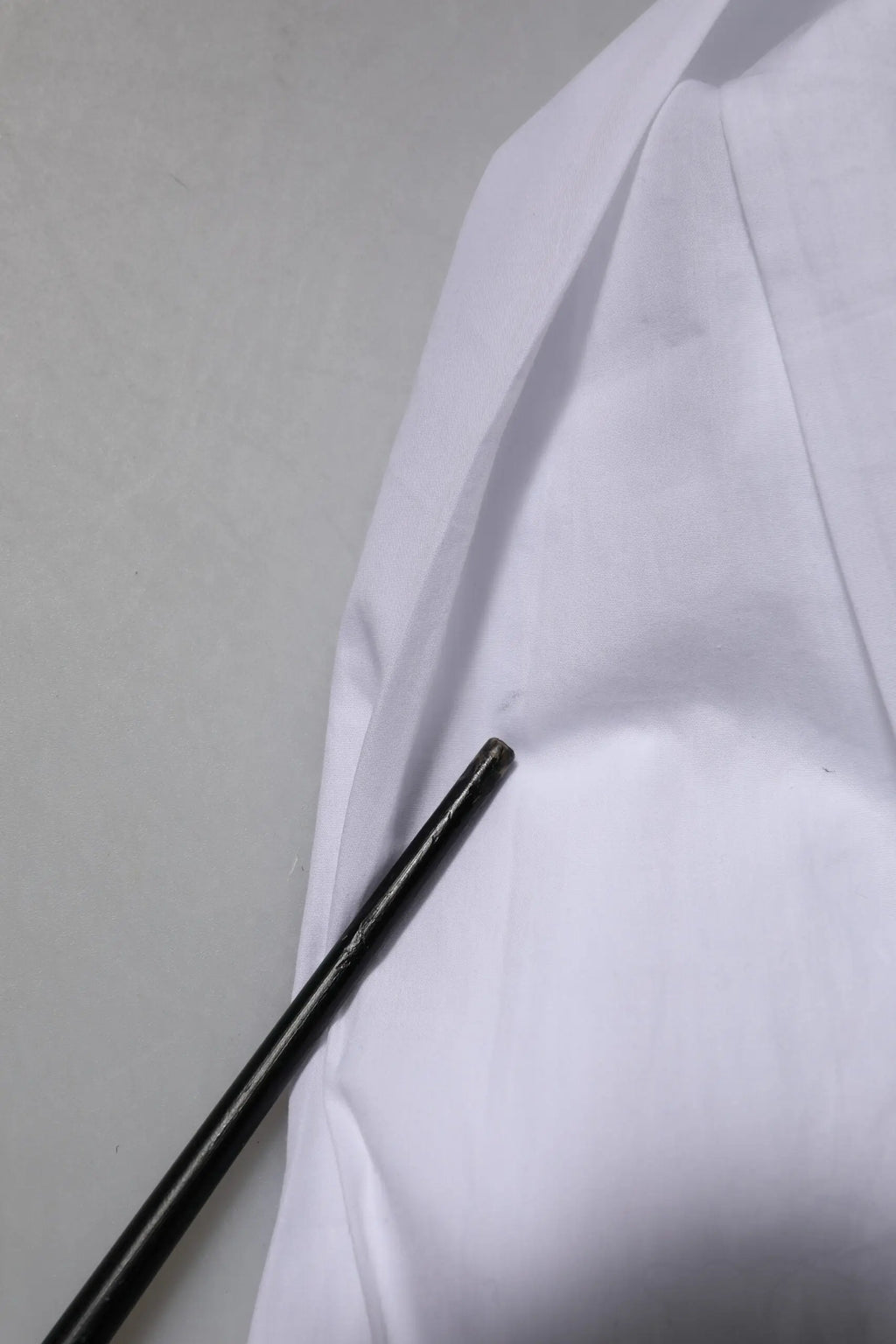Objet cylindrique noir posé sur tissu blanc à côté d’une chemise formelle en coton blanc à manches longues Dolce & Gabbana gold