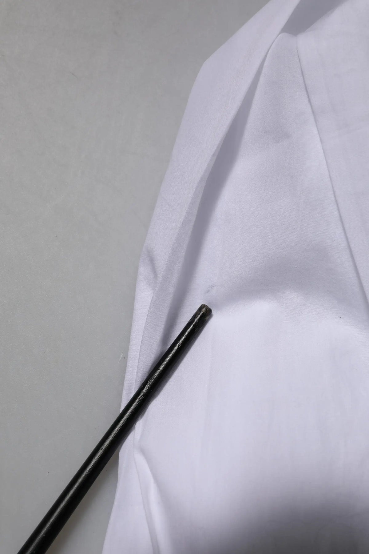 Objet cylindrique noir posé sur tissu blanc à côté d’une chemise formelle en coton blanc à manches longues Dolce & Gabbana gold