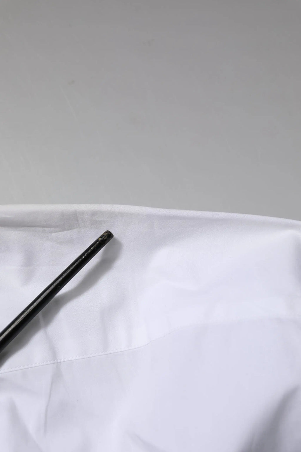 Objet cylindrique noir avec surface texturée posé sur tissu blanc près d’une chemise blanche en coton Dolce & Gabbana