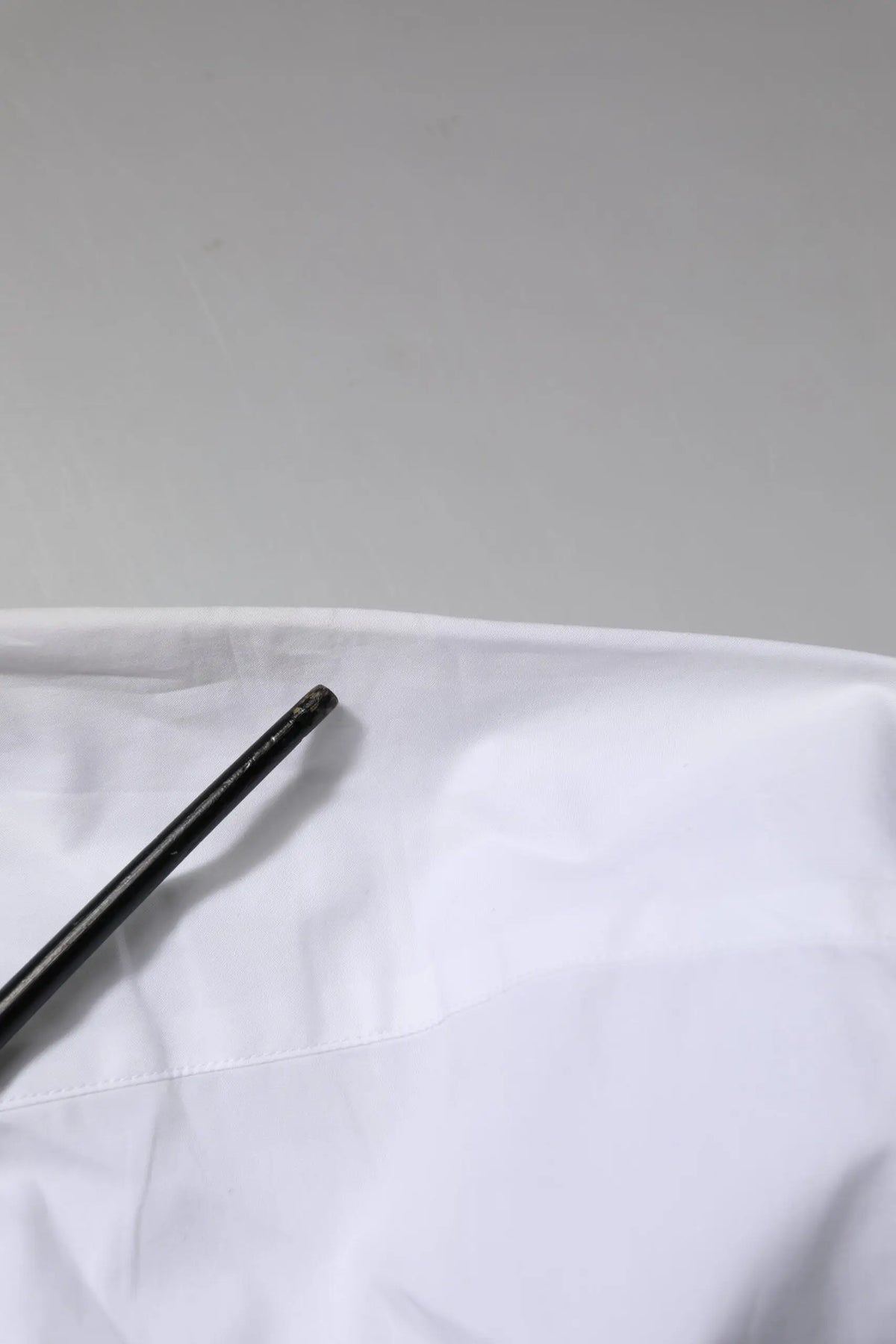 Objet cylindrique noir avec surface texturée posé sur tissu blanc près d’une chemise blanche en coton Dolce & Gabbana