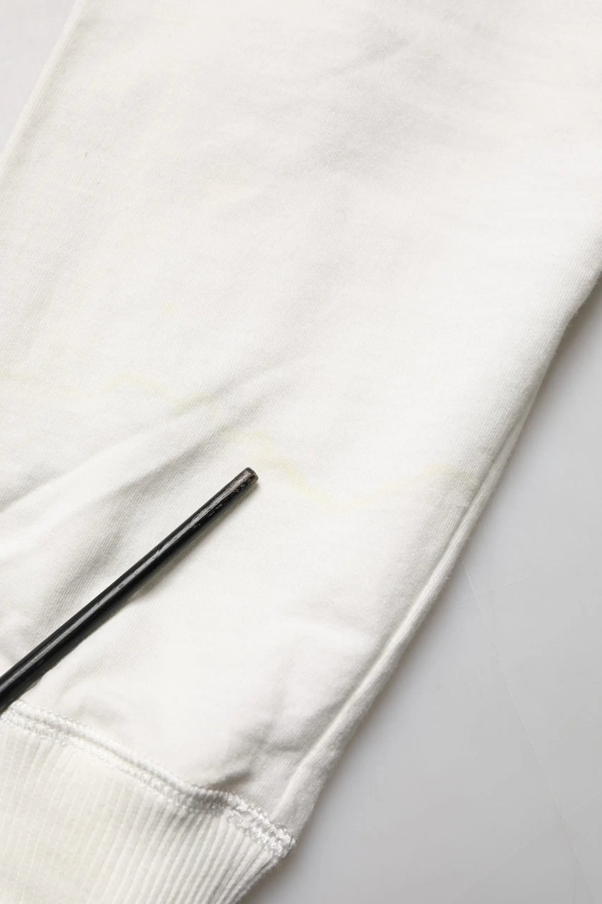 Un stylo noir mince repose en diagonale sur la manche en tissu blanc doux du sweat à capuche en coton dolce & gabbana