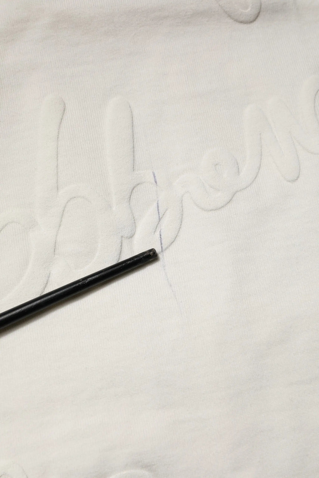 Crayon noir reposant sur tissu blanc avec lettrage brodé sur t shirt dolce & gabbana blanc en coton embossé