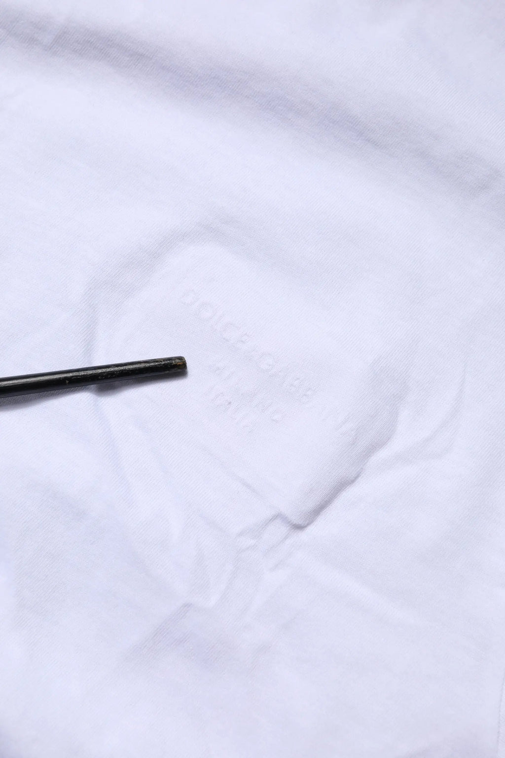 Crayon cylindrique noir reposant sur tissu blanc du t-shirt dolce & gabbana en coton blanc avec logo patch
