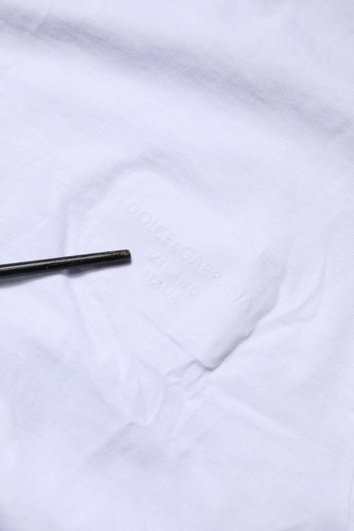 Crayon cylindrique noir reposant sur tissu blanc du t-shirt dolce & gabbana en coton blanc avec logo patch