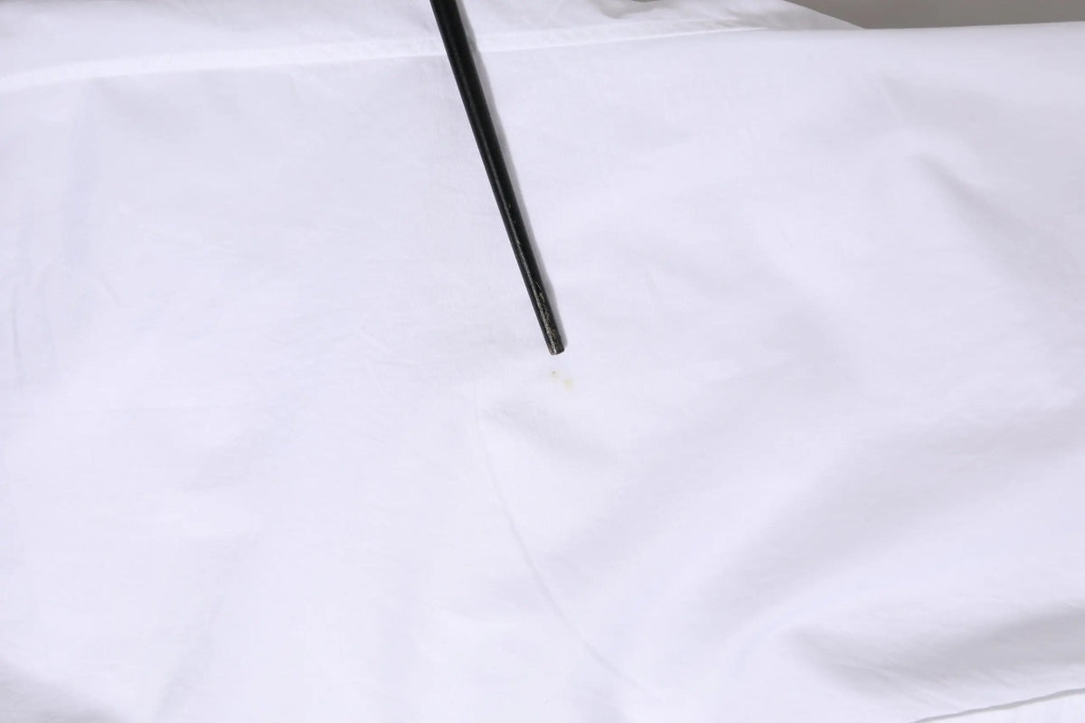Un repose-baguettes noir élégant posé en diagonale sur un tissu blanc lisse dune chemise formelle blanche en coton dolce et gabbana