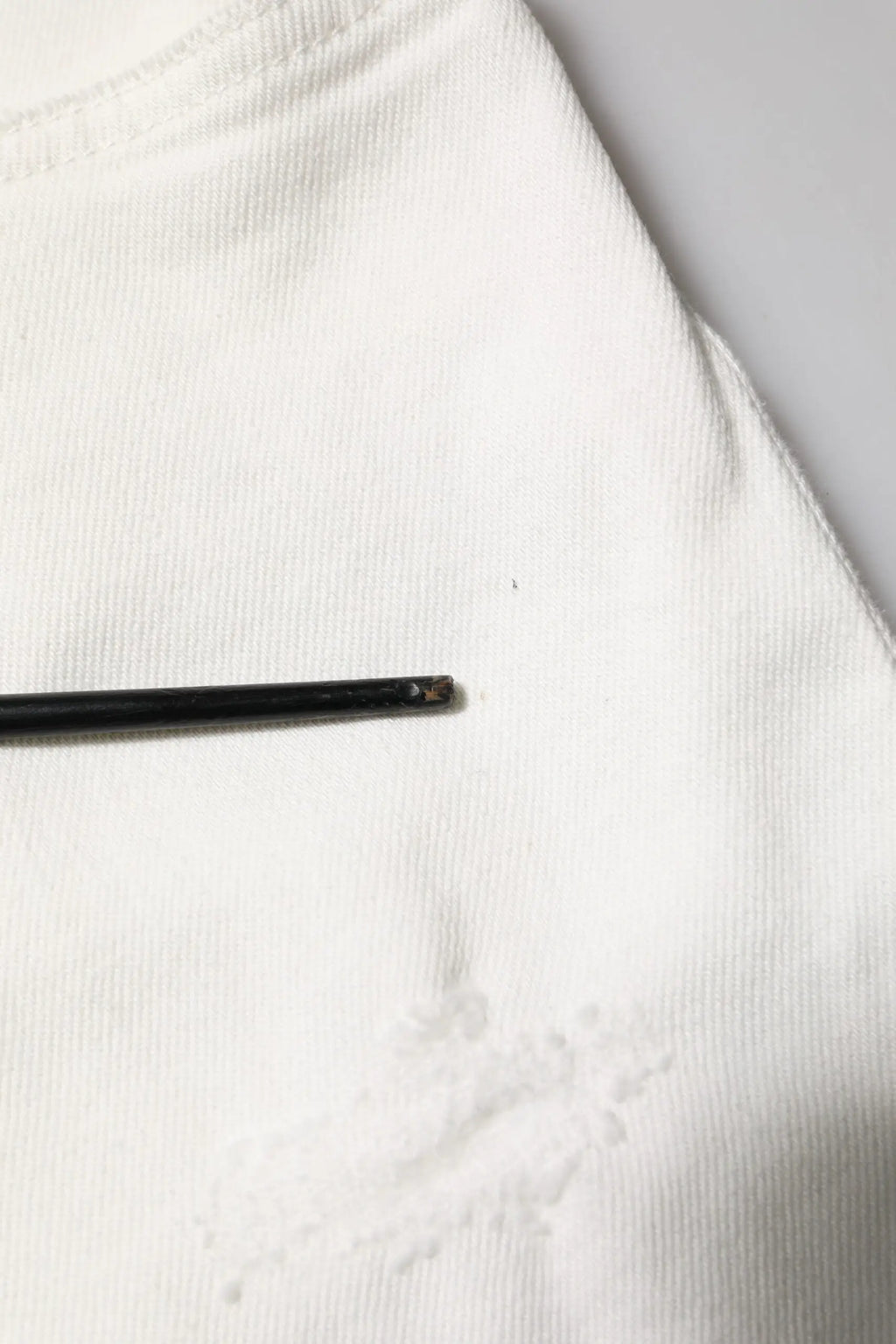 Un stylo noir mince mat posé horizontalement sur un jean denim homme blanc en coton loose de dolce & gabbana
