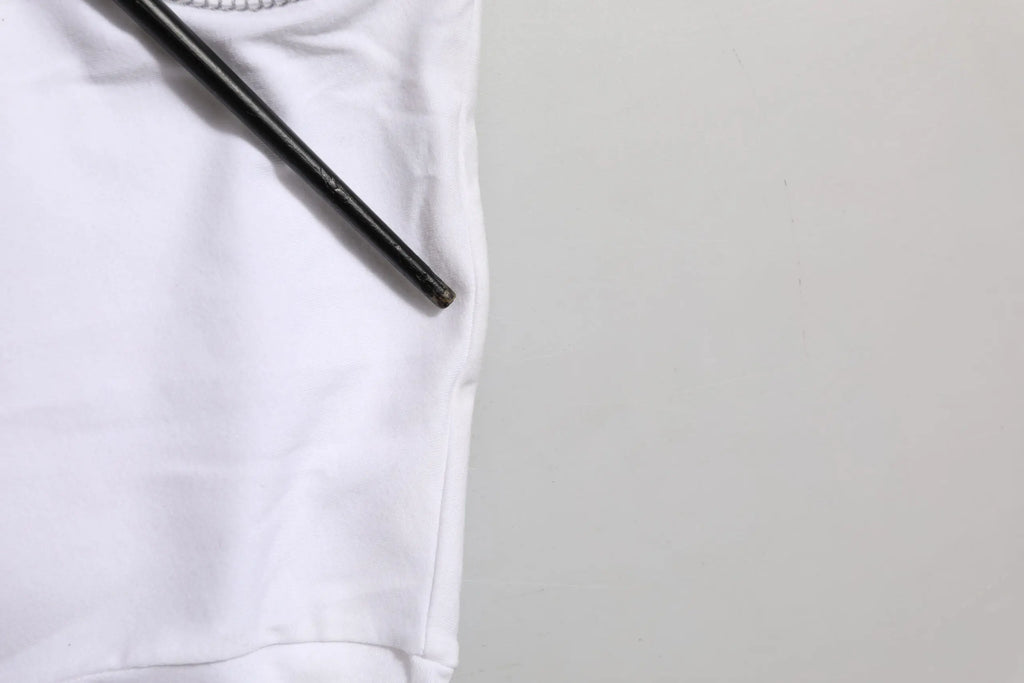 Un crayon noir mince repose en diagonale sur le tissu blanc lisse d un t shirt dolce & gabbana en coton pour homme
