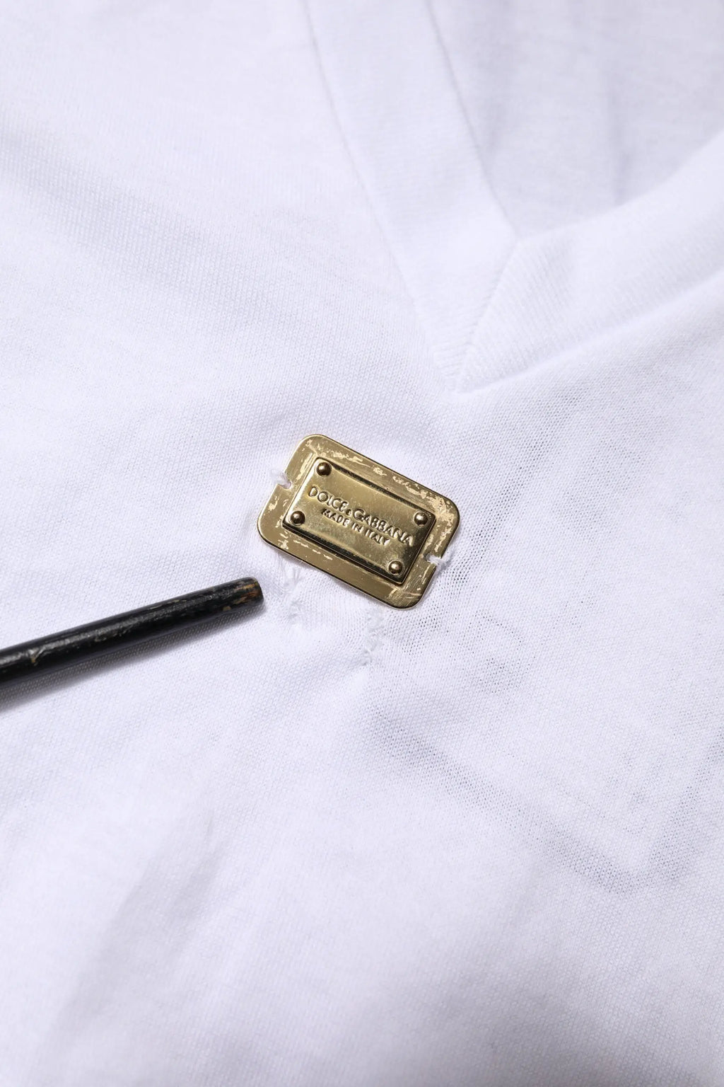 Plaque rectangulaire en métal doré avec dolce & gabbana gravé sur tissu blanc dun t-shirt blanc en coton col v à manches courtes