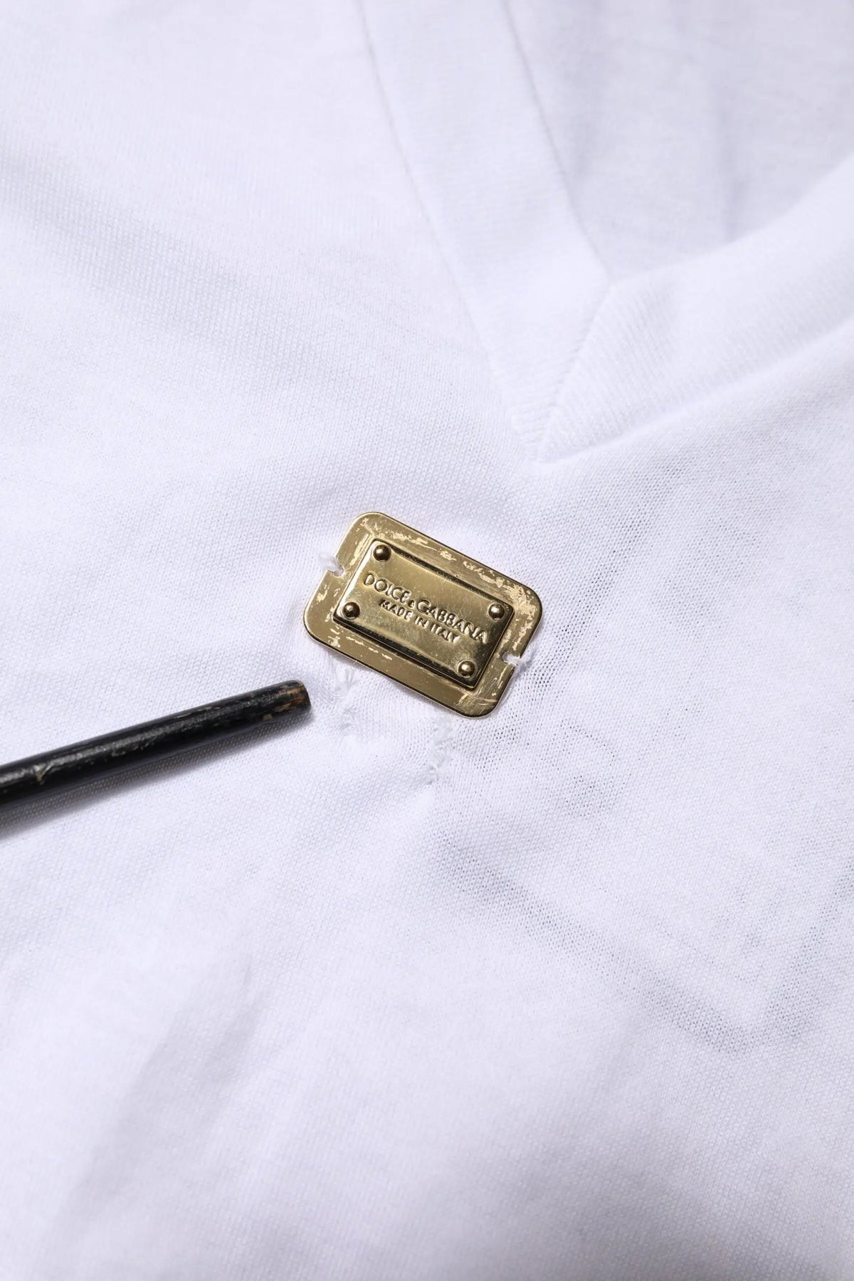Plaque rectangulaire en métal doré avec dolce & gabbana gravé sur tissu blanc dun t-shirt blanc en coton col v à manches courtes