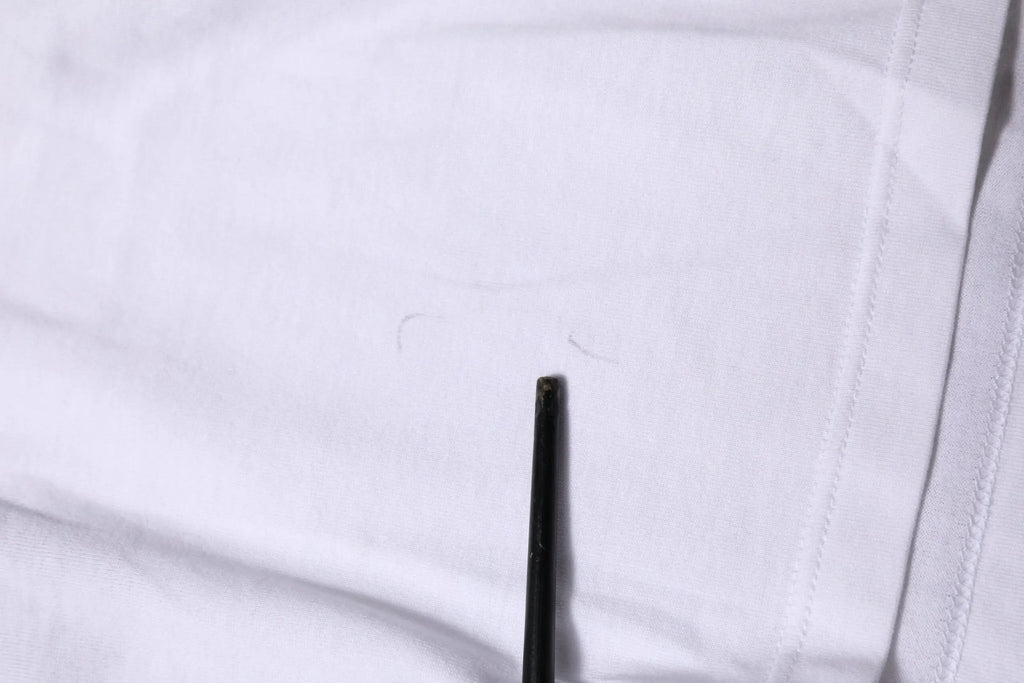Un crayon noir pointe contre un tissu blanc sur un t-shirt court blanc en coton dolce & gabbana