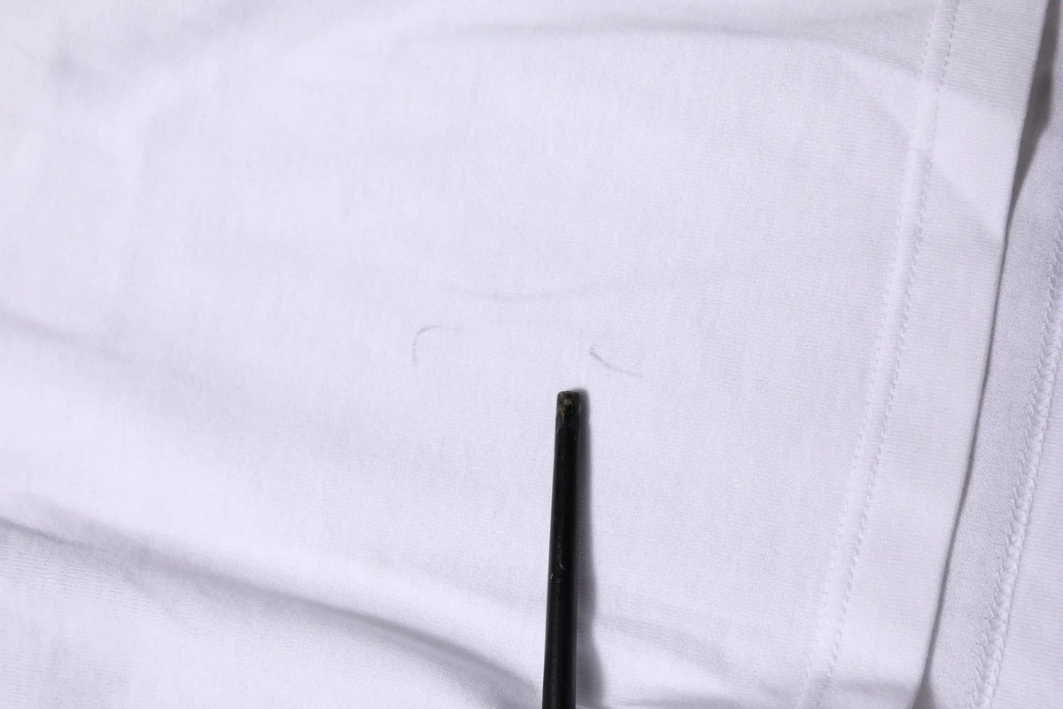 Un crayon noir pointe contre un tissu blanc sur un t-shirt court blanc en coton dolce & gabbana