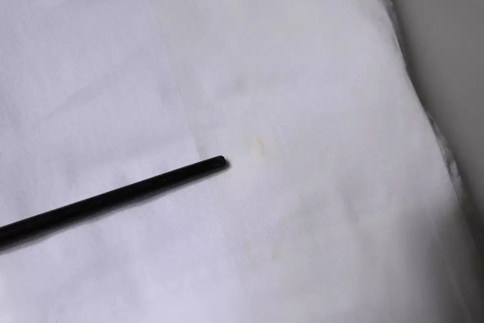 Crayon cylindrique noir posé sur une surface blanche avec un pantalon skinny blanc en coton dolce & gabbana