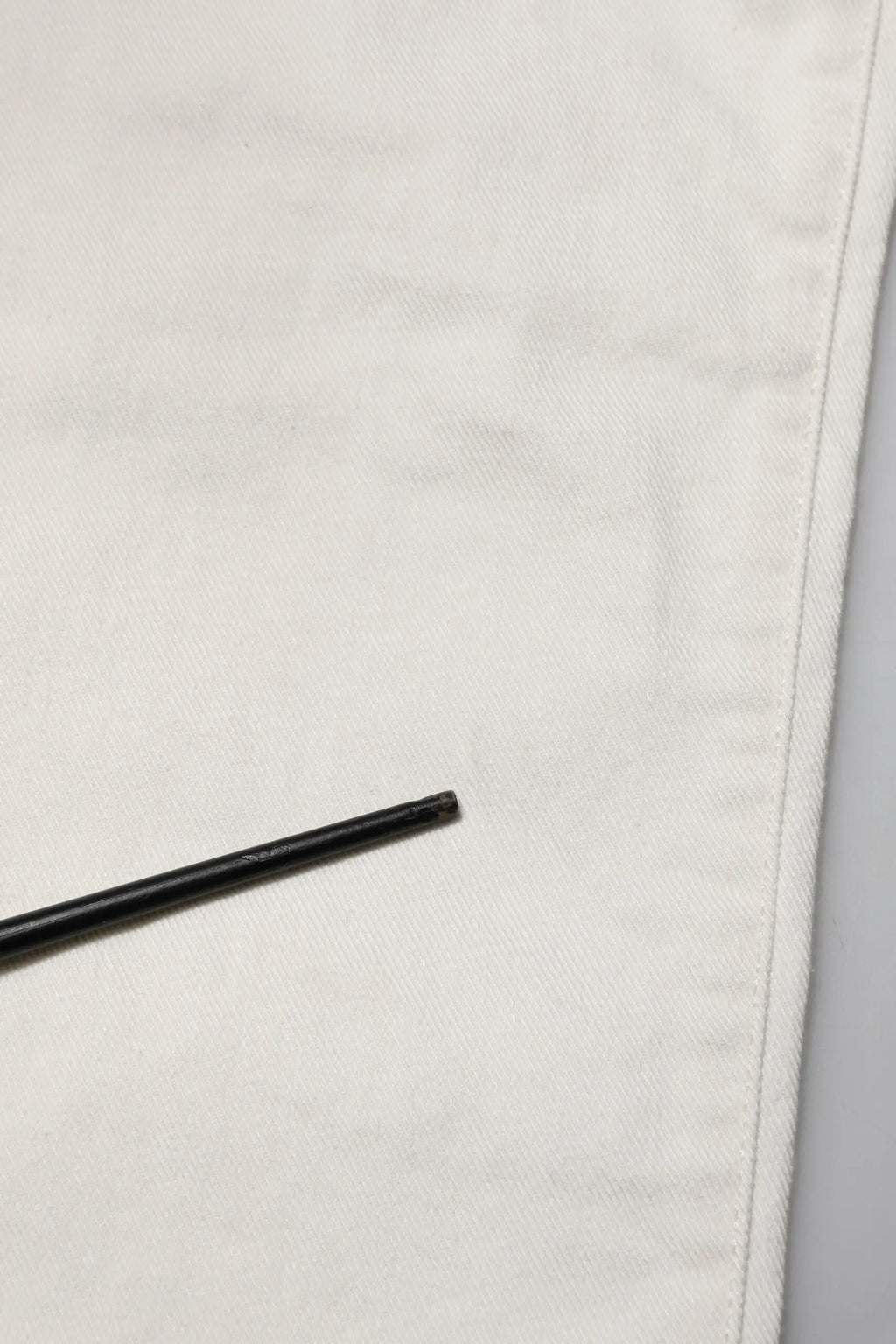 Stylo cylindrique noir posé sur tissu blanc à côté d un jean skinny homme en coton blanc dolce & gabbana