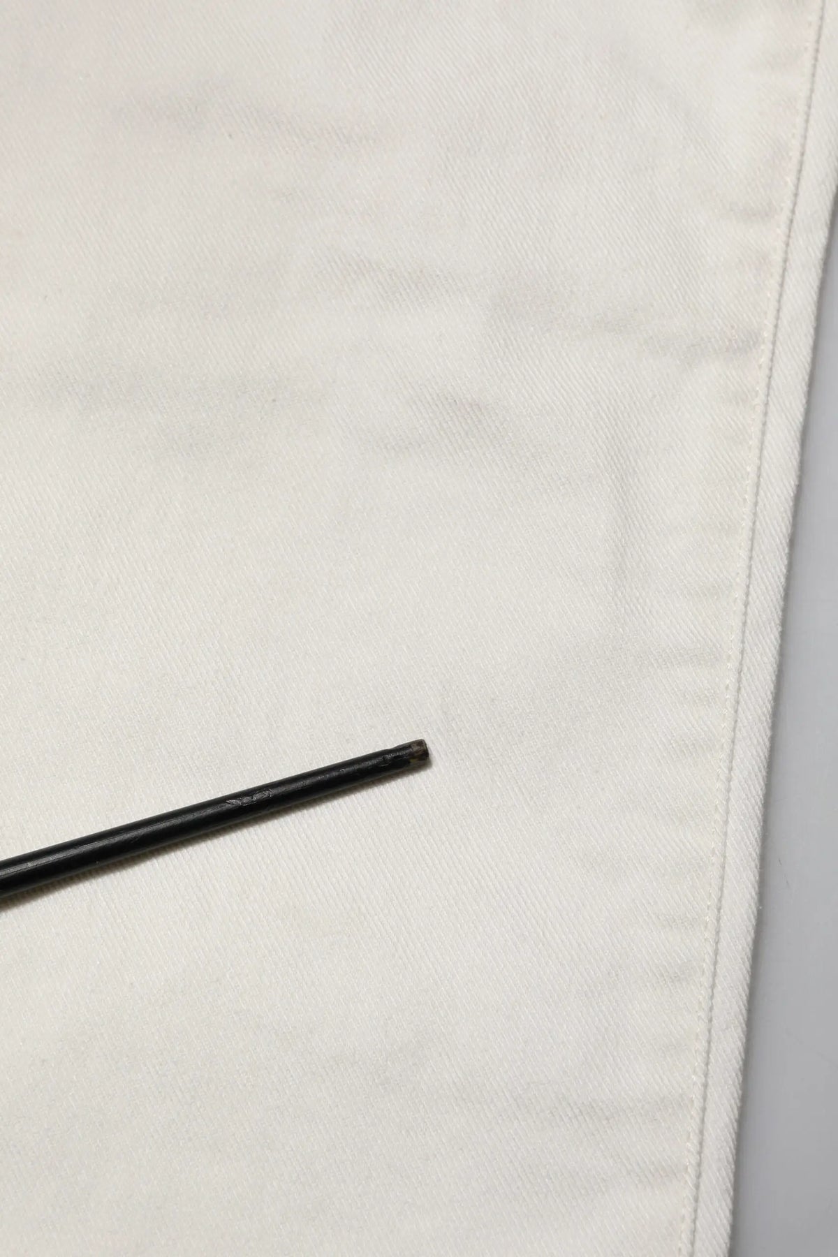 Stylo cylindrique noir posé sur tissu blanc à côté d un jean skinny homme en coton blanc dolce & gabbana