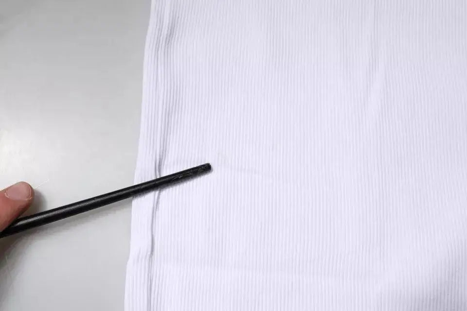 Un crayon noir posé contre un tissu blanc côtelé du débardeur sans manches rond en coton dolce & gabbana