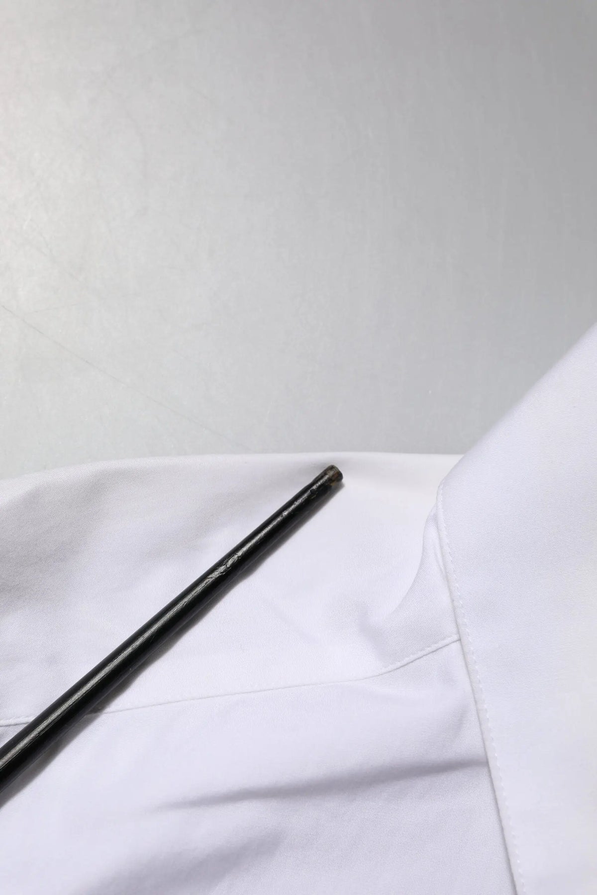 Objet cylindrique noir mat posé sur tissu blanc à côté d’une chemise blanche à col ornée de cristaux Dolce & Gabbana