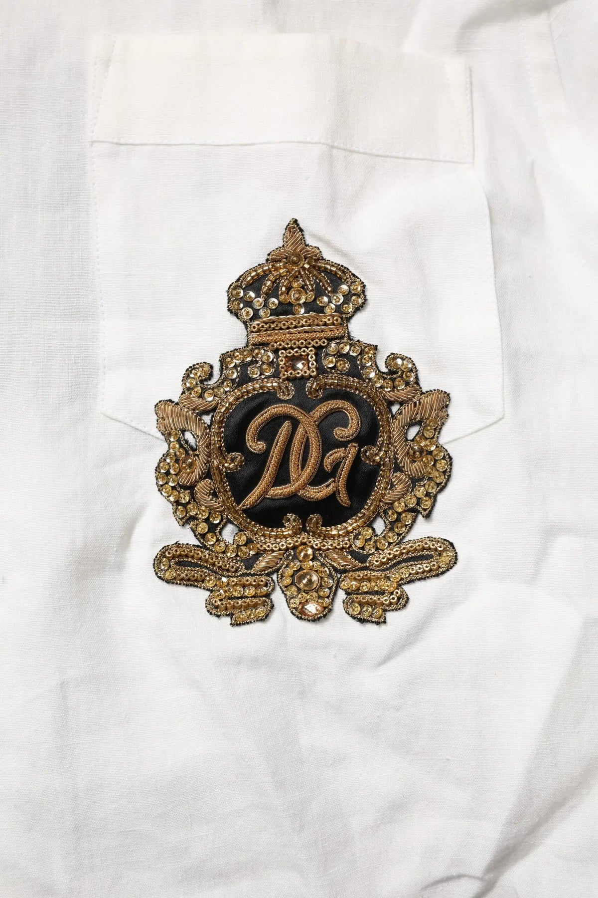 Patch logo dolce gabbana brodée or avec perles et motif couronne sur tissu noir pour chemise formelle blanche dg crown