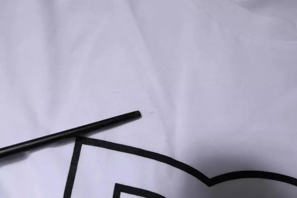 Objet cylindrique noir posé sur tissu blanc avec motif géométrique noir du t-shirt col rond coton dolce & gabbana blanc dg logo
