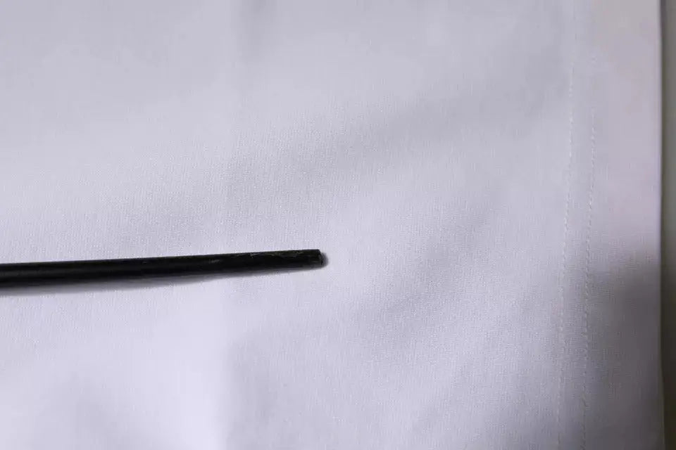 Objet cylindrique noir mat posé horizontalement sur surface blanche avec t shirt dolce gabbana blanc logo dg col rond manches courtes