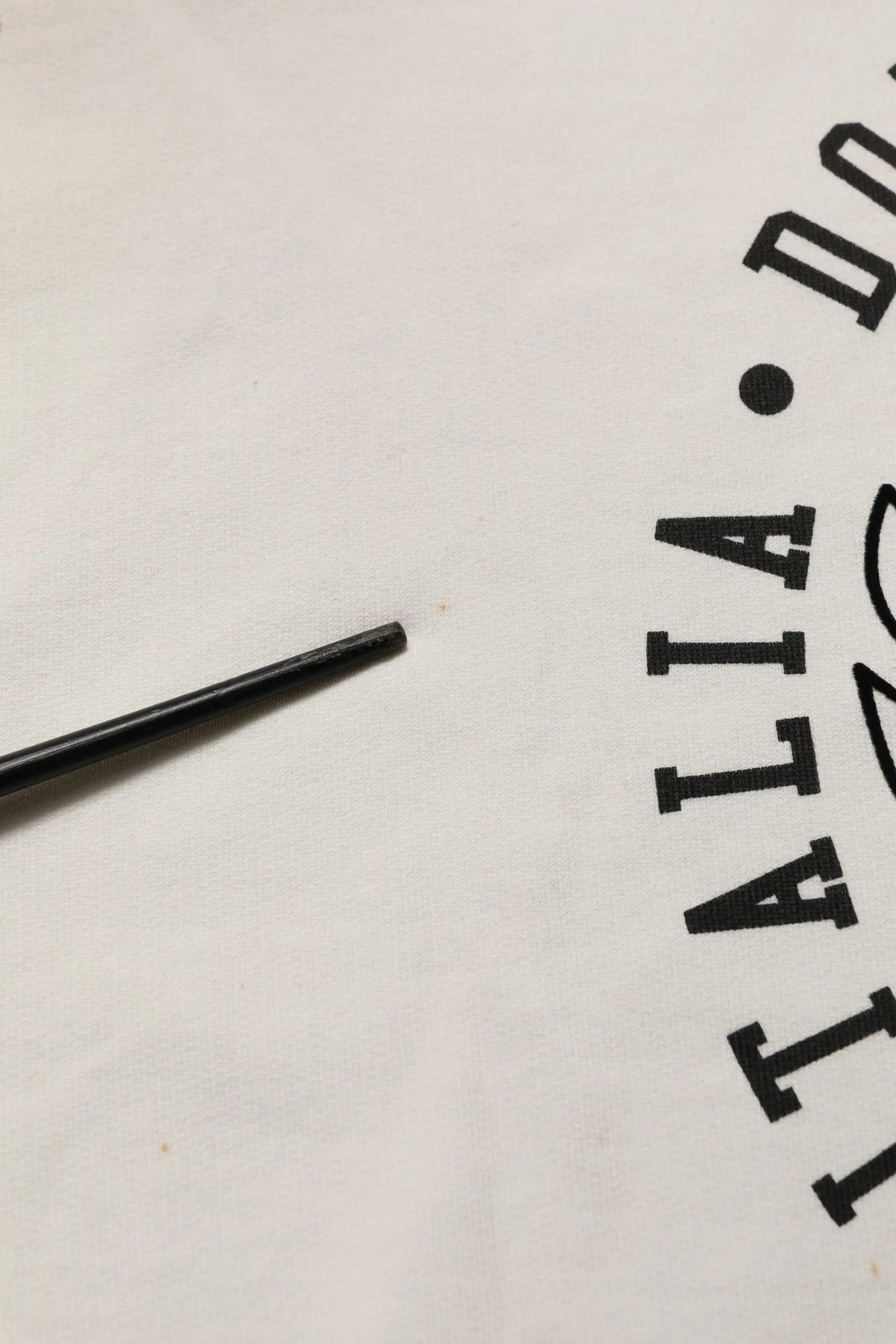 Une paille noire cylindrique posée sur un sweat blanc dolce & gabbana avec logo dg et texte partiel italia