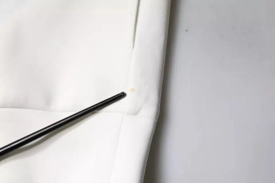 Bâtonnets noirs reposant sur un tissu blanc à côté d’un sweat à capuche blanc dolce & gabbana avec logo dg homme