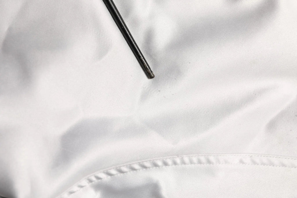 Un objet cylindrique noir élégant posé sur un tissu blanc doux en polyester dans la veste bomber dolce & gabbana blanche dg logo