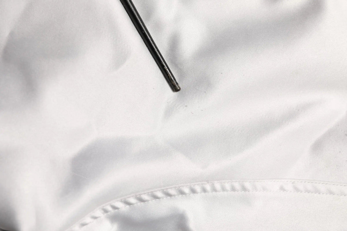 Un objet cylindrique noir élégant posé sur un tissu blanc doux en polyester dans la veste bomber dolce & gabbana blanche dg logo