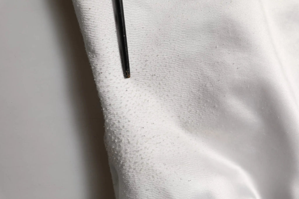 Une aiguille noire repose sur un tissu blanc texturé du blouson bomber en jersey polyester blanc dolce gabbana dg logo
