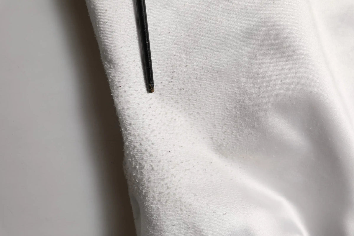 Une aiguille noire repose sur un tissu blanc texturé du blouson bomber en jersey polyester blanc dolce gabbana dg logo