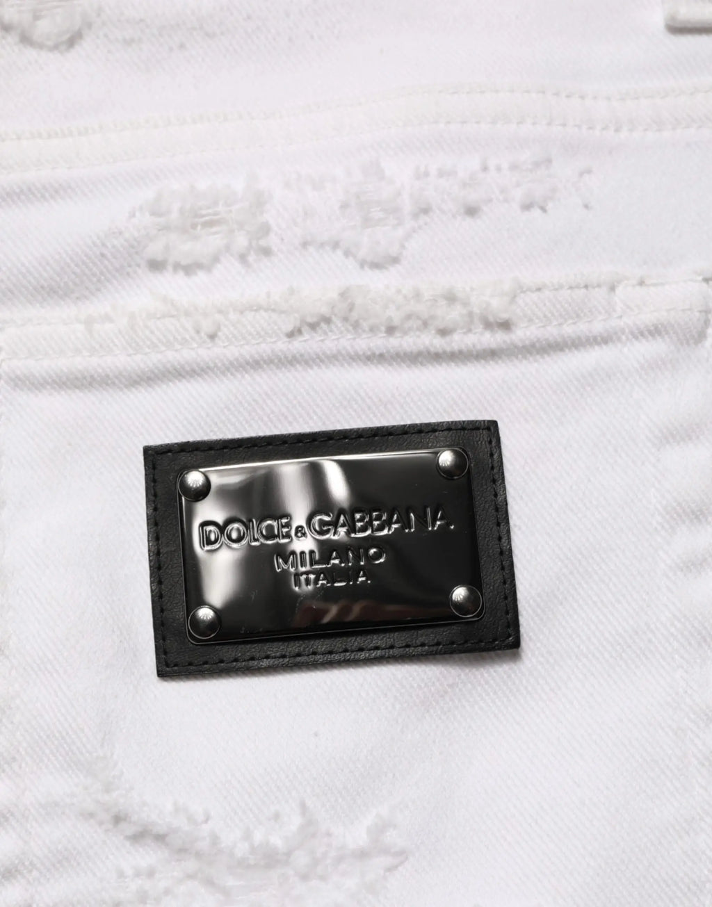 Patch en cuir noir avec plaque métallique argentée dolce & gabbana milano italia cousue sur denim blanc déchiré