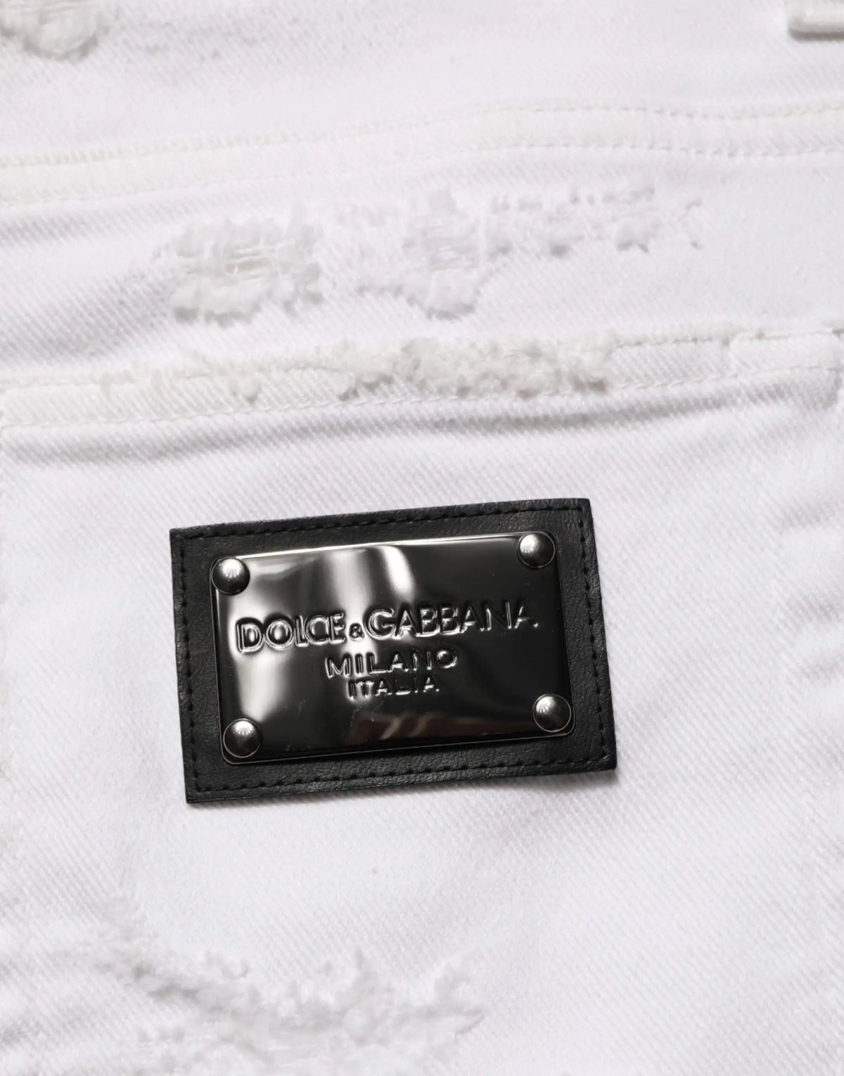 Patch en cuir noir avec plaque métallique argentée dolce & gabbana milano italia cousue sur denim blanc déchiré