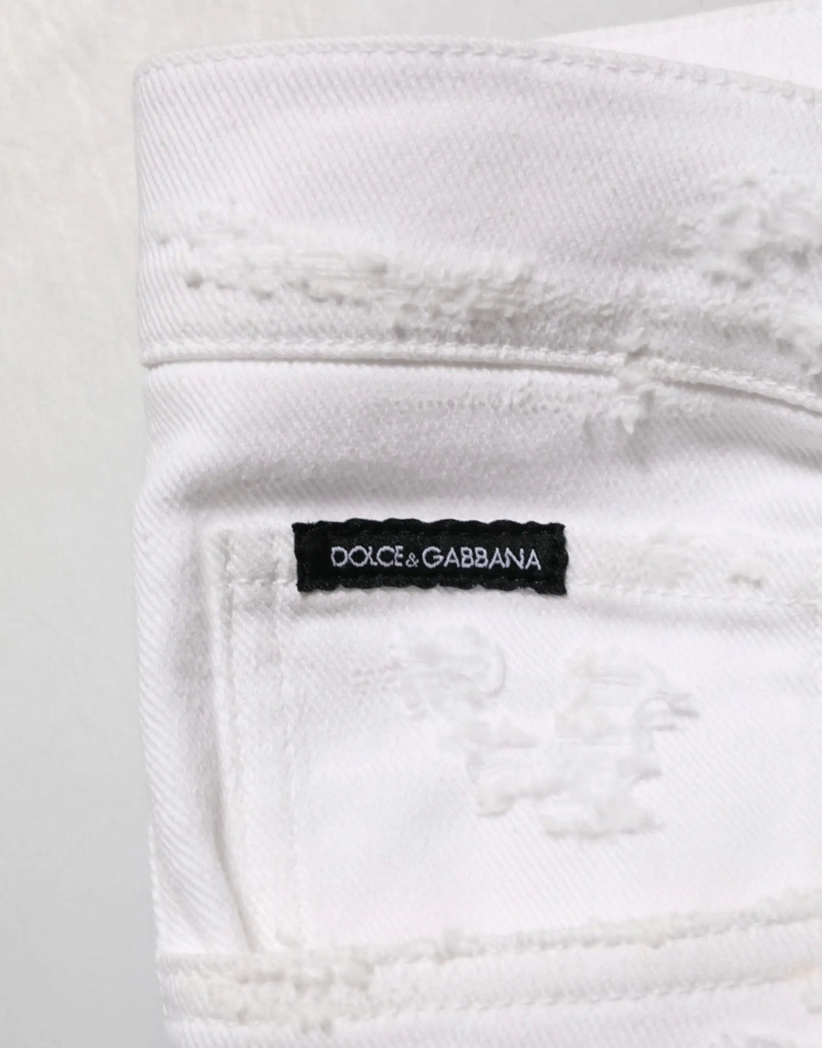 Jean denim blanc déchiré dolce gabbana avec étiquette noire visible sur le dos du produit