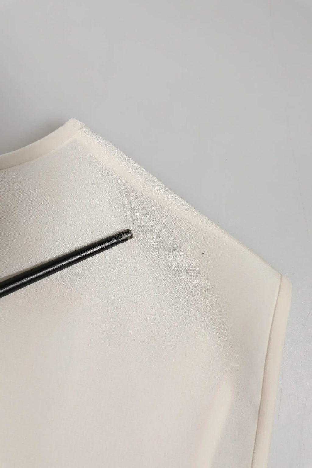 Un stylo noir élégant repose en diagonale sur le tissu blanc orné de cristaux du top fairy embellished de Dolce & Gabbana