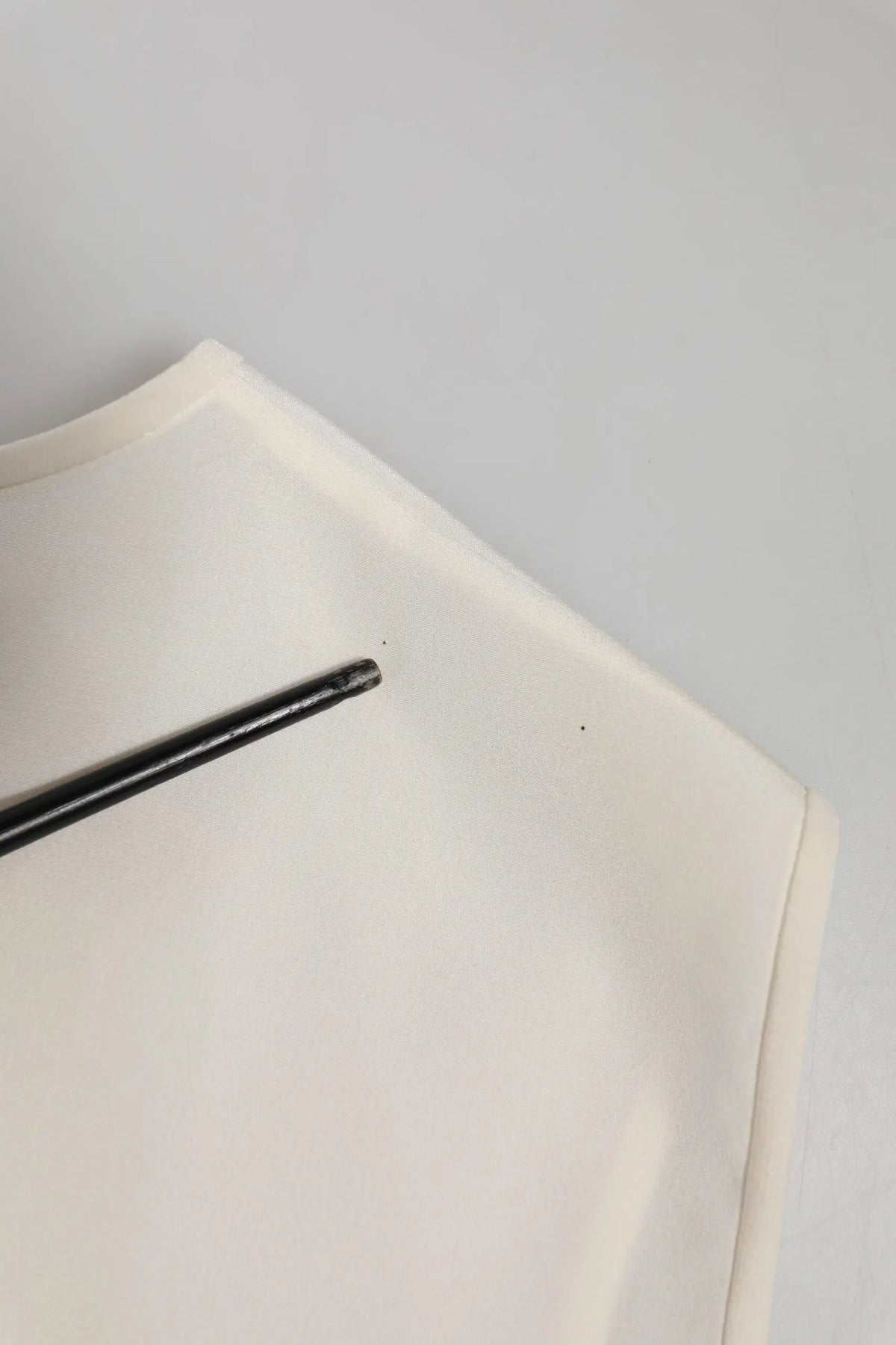 Un stylo noir élégant repose en diagonale sur le tissu blanc orné de cristaux du top fairy embellished de Dolce & Gabbana