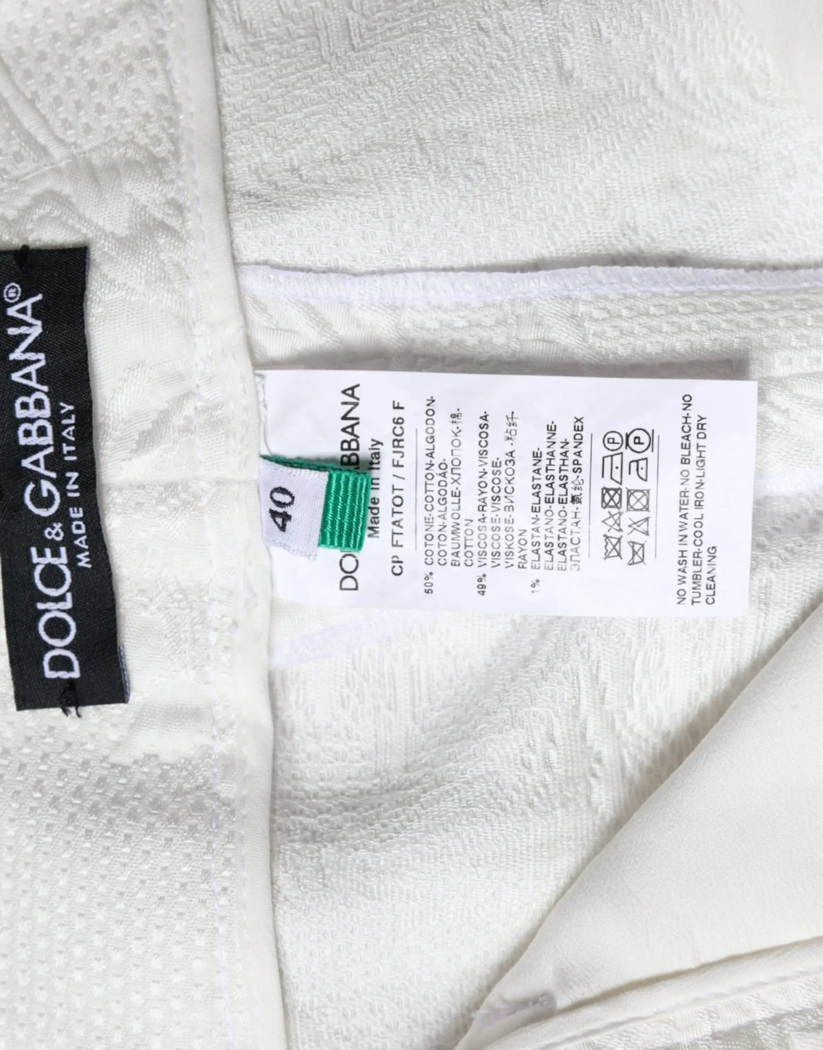 Étiquette en coton blanc texturé avec marque dolce & gabbana et instructions d’entretien noir sur pantalon blanc brocart floral