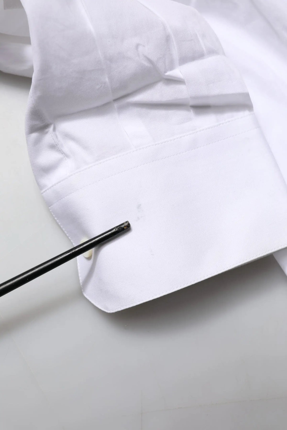 Un outil cylindrique noir élégant avec une extrémité texturée posé contre la manchette blanche en popeline dorée white gold de la chemise formelle dolce & gabbana