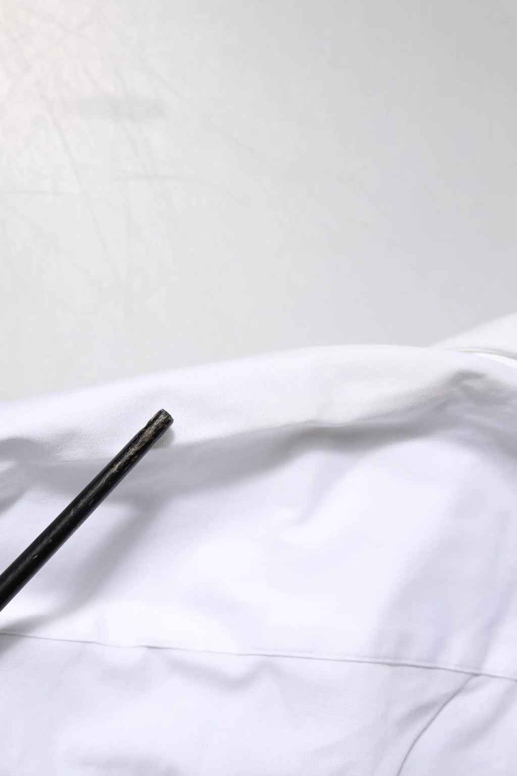 Un crayon noir mat élégant repose en diagonale sur un tissu en coton blanc de la chemise Dolce & Gabbana white gold