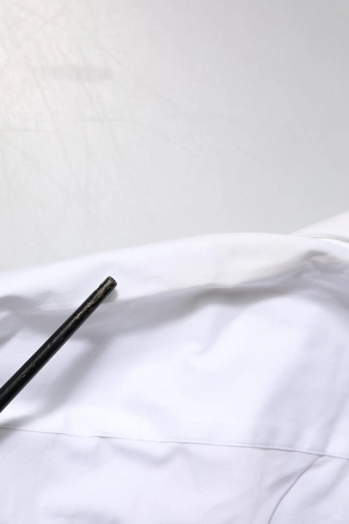 Un crayon noir mat élégant repose en diagonale sur un tissu en coton blanc de la chemise Dolce & Gabbana white gold